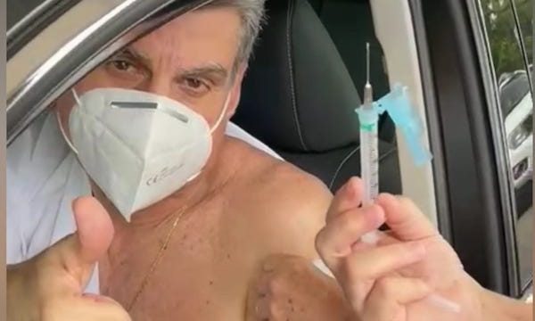 Romero Jucá dentro do carro faz sinal de positivo com o polegar levantado após tomar a vacina contra a covid-19. Ao seu lado, a profissional de saúde mostra a seringa vazia.