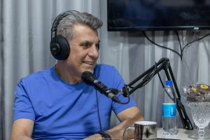 Romero Jucá em estúdio, com camisa azul e sorrindo ao falar no microfone.